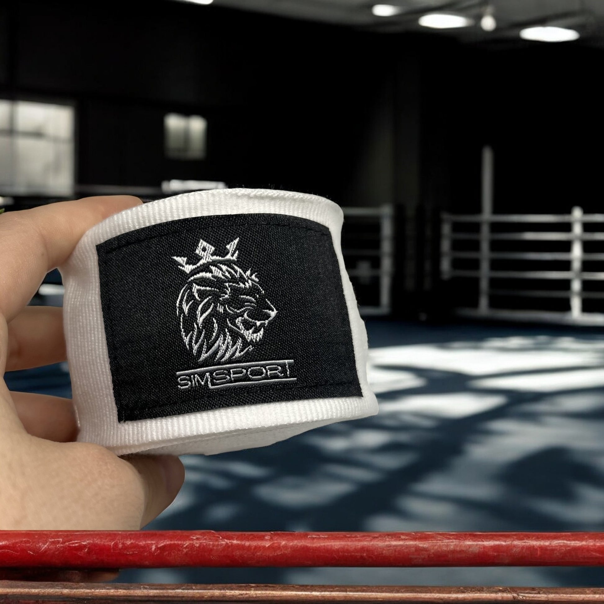 Bandes de boxe SIMSPORT couleur blanc portées avec un ring de boxe en arrière plan