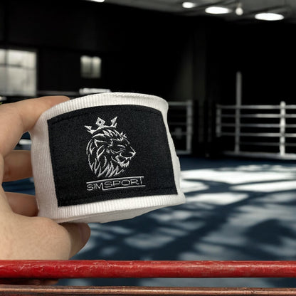 Bandes de boxe SIMSPORT couleur blanc portées avec un ring de boxe en arrière plan