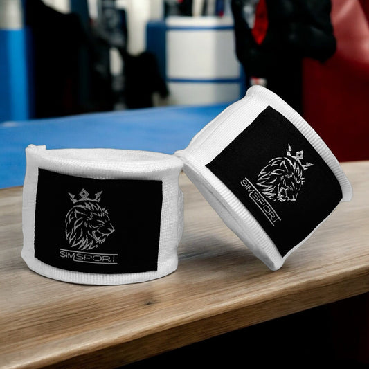 Bandes de boxe SIMSPORT couleur blanc posées sur une table en bois avec un ring de boxe en arrière plan