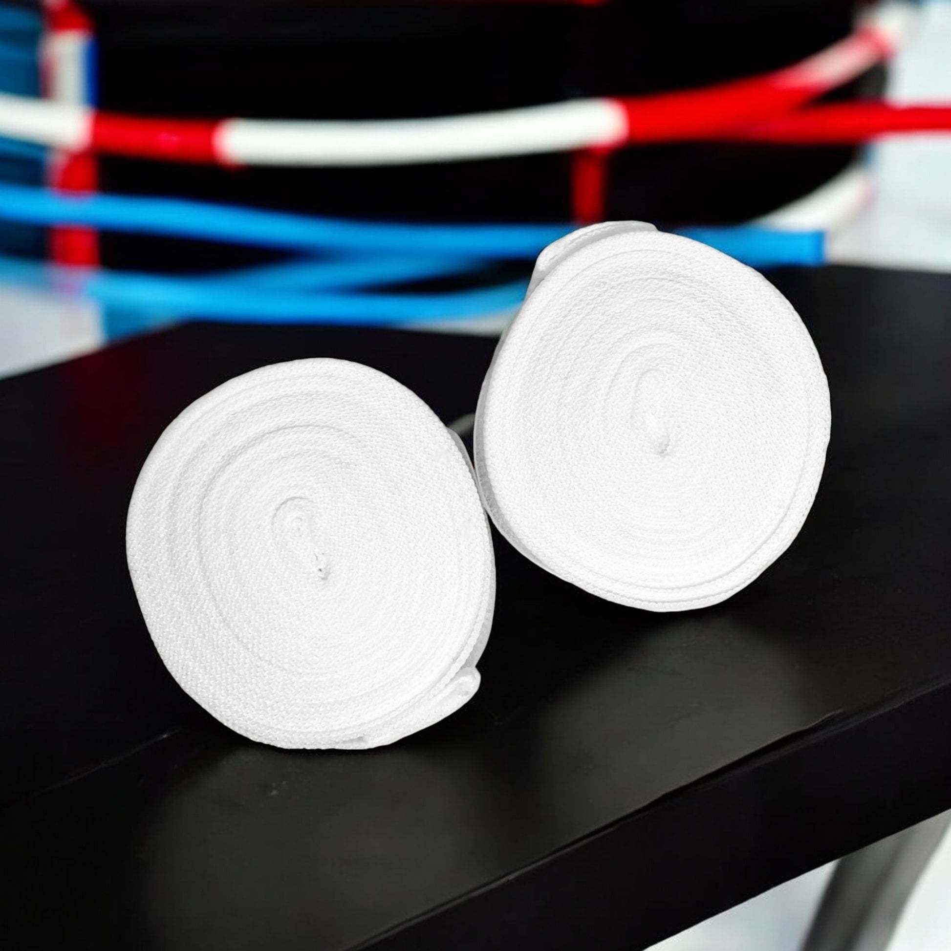 Bandes de boxe SIMSPORT couleur blanc posées sur une table noir avec un ring de boxe en arrière plan