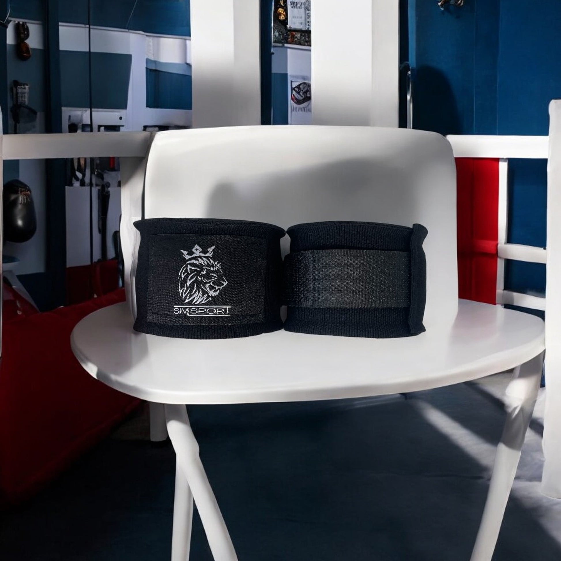 Bandes de boxe SIMSPORT couleur noir posées sur un tabouret ring de boxe en arrière plan, sacs de frappe