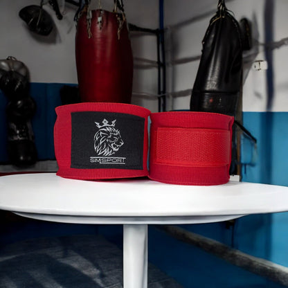 Bandes de boxe SIMSPORT couleur rouge posées sur une table blanche salle de boxe en arrière plan, sacs de frappe