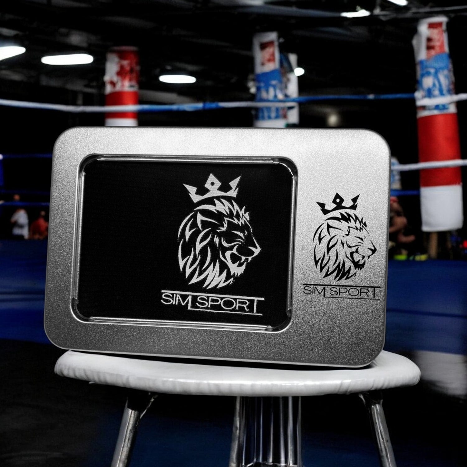 Pad de protection mains (métacarpes) posés sur un tabouret dans un ring de boxe, offert avec sa boîte métallique, couleur noir, sacs de frappe boxe en arrière plan