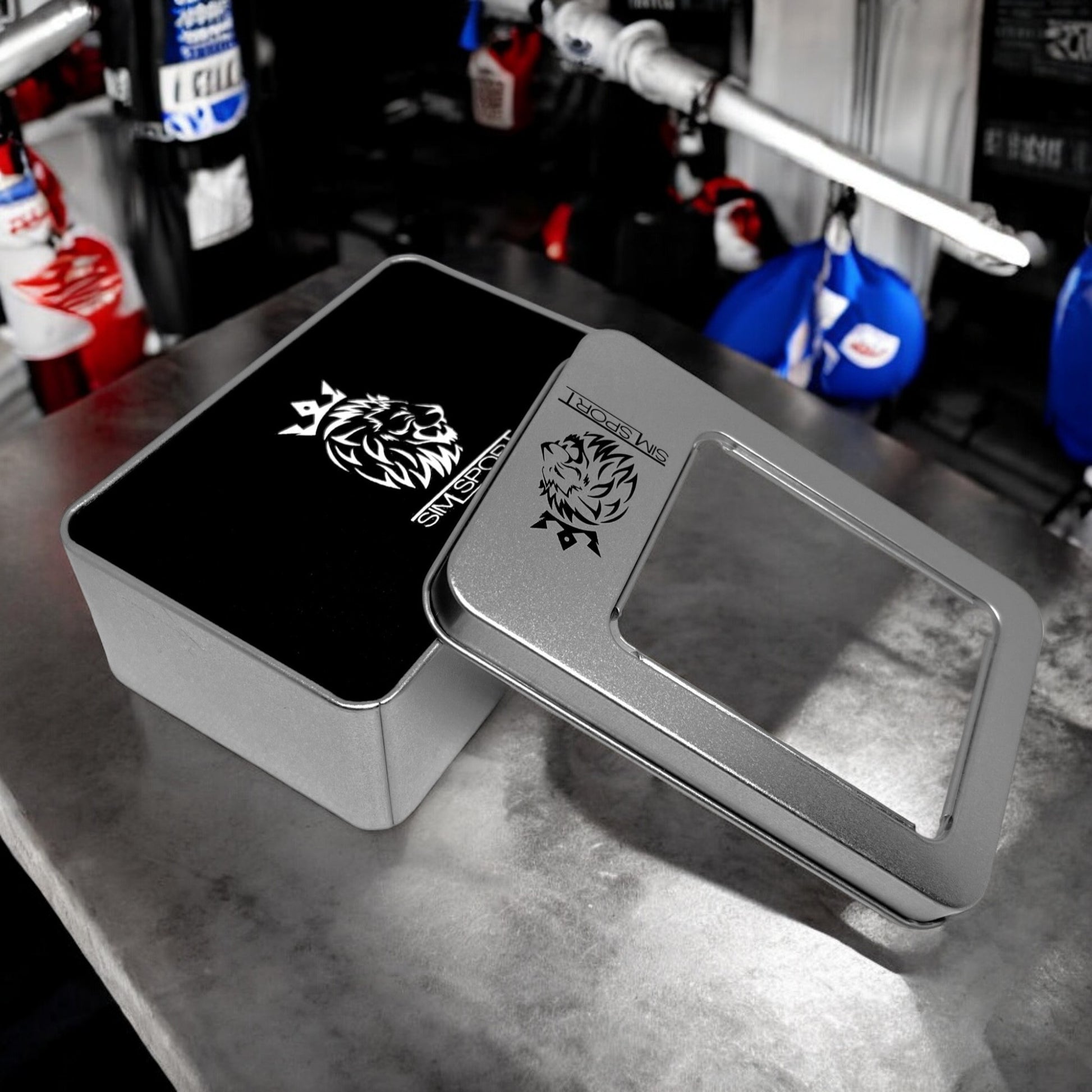 Pad de protection mains (métacarpes) posés sur une table grise, offert avec sa boîte métallique, couleur noir, sacs de frappe boxe en arrière plan